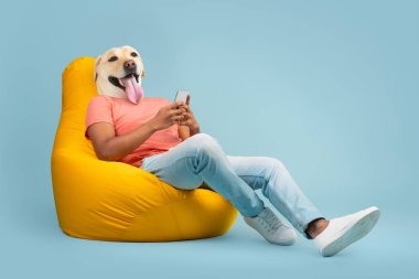 A man is comfortably lounging in a vibrant yellow bean bag chair, engrossed in his phone. The amusing twist is that his head is replaced by that of a cheerful dog clipart