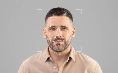 Gri bir arkaplanın önünde duran bir adam yüz tanıma teknolojisi görüntüsüyle meşgul oluyor..