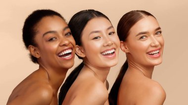 Deri ve Vücut Bakımı. Beyaz arka planda duran ve kameraya gülümseyen üç çok ırklı kadın. Stüdyo Çekimi, Panorama