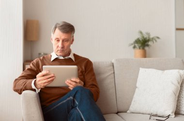 Son sınıf öğrencisi, Dijital Tablet okuyarak iş haberleri okuyor. İçerideki koltukta oturuyor. Seçici Odaklanma, Boş Alan