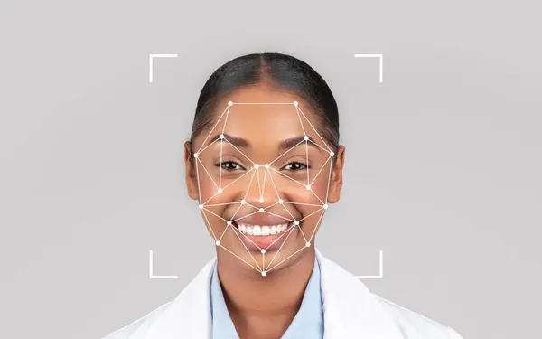 Stock image A happy black lady healthcare professional smiles while demonstrating facial recognition technology in a clinical setting.