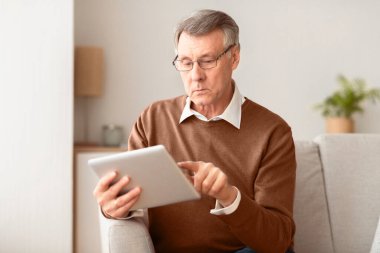 Ciddi Yaşlılar Dijital Tablet Kullanarak İnternet Tarama ve İş Haberleri Okuma İçerideki Koltukta Oturuyor. Seçici Odaklanma