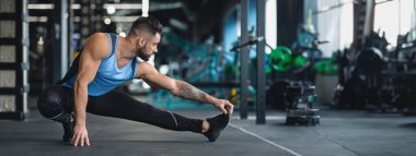 Bir adam antrenman sırasında esneklik ve dayanıklılığa odaklanarak spor salonunda yan esneme hareketleri yapıyor.