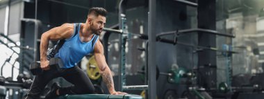 Güç egzersizi. Spor salonunda dambılla spor yapan yakışıklı bir sporcu, boş alan, web pankartı.