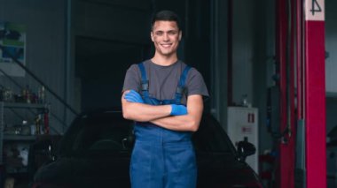 Araba tamircisinin portresi, atölyede arabanın yanında poz veriyor, kameraya gülümsüyor.