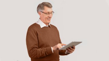 Harika bir uygulama. İçerik Kıdemli Adam Tablet Bilgisayar kullanarak Gri Arkaplanda Duran İnternet 'i tarıyor. Stüdyo Çekimi, Panorama