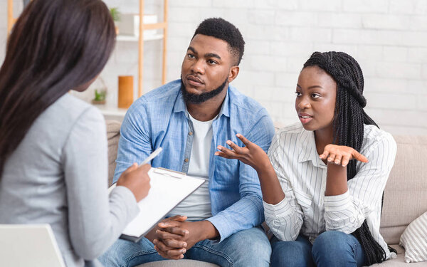 Marital psychotherapy concept. Young afro couple with relationship problems sitting at therapy session with psychologist