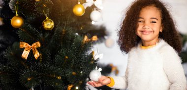 Noel zamanı. Sevimli Afrikalı Amerikalı kız evde Noel ağacının yanında gülümsüyor, boşlukta.