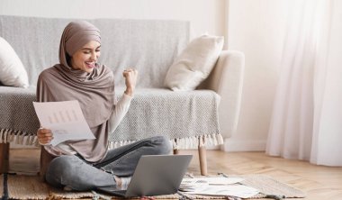 Joyful Muslim Woman Celebrating Business Success While Working With Papers And Laptop At Home, Finished Importrant Project