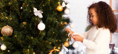 Noel geleneği. Evde Noel ağacı süsleyen küçük afro kız, boş yer.