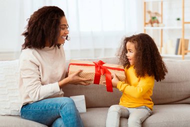 Afrikalı Amerikalı anne küçük kızına hediye veriyor. Doğum gününü evde koltukta oturarak kutluyor. Aile Tatili Konsepti