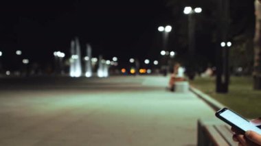 Şehir parkının fıskiyeli görüntüsü ve cep telefonunda gezinen yalnız adam, kapat.