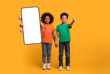İki neşeli siyah çocuk, parlak sarı bir arkaplanda el ele tutuşup gülümsüyor. Bir çocuk boş bir akıllı telefon sergilerken, diğeri heyecanını dışa vuruyor..