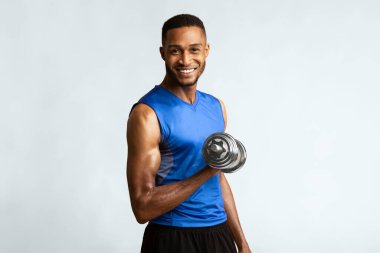Fitness kulübü reklamı. Turuncu stüdyo duvarının üzerinden izole edilmiş halterli biseps bisepsi yapan mutlu siyah adam, kamera telif uzayına bakıyor.