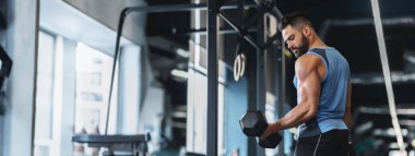 A man focuses on lifting a dumbbell, showcasing his strength in an indoor gym setting, copy space clipart