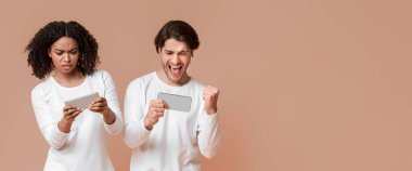 Boş zaman aktiviteleri. Akıllı telefonlarda video oyunu oynayan, birbirleriyle yarışan, kazanan, sarı arka planda olan çok ırklı çift.