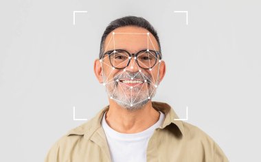 Gözlüklü, gülümseyen bir adam parlak bir stüdyoda duruyor, yüzünde yüz tanıma yazısıyla modern teknolojiyi ön plana çıkarıyor..