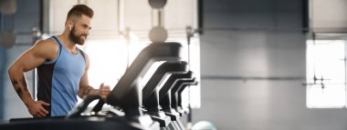 Zevkle koşuyor. Modern kablosuz kulaklık genç yakışıklı adam gülümseyerek, spor salonunda koşu bandı üzerinde çalışan, boş alan