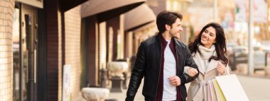 Bir çift birlikte yürür, gülümser ve alışveriş torbaları taşır, günlük kıyafetler giyer, güneşli bir günde eğlenir, boşluğu kopyalarlar.