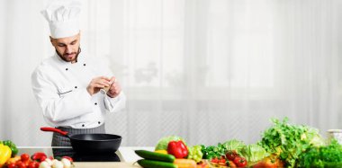 Cooking Food Concept. Professional Chef Adding Pepper In Frying Pan Seasoning Dish Standing In Kitchen Indoor. Selective Focus