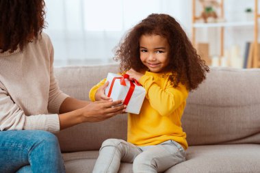 Çocukların doğum günü. Şirin Afrikalı küçük kız paketlenmiş hediyesini açıyor. Annesiyle birlikte evde kanepesinde oturuyor..