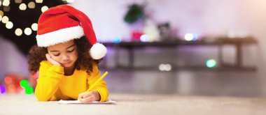 Noel Baba şapkalı güzel Afrikalı kız Noel ağacının yanında Noel Baba 'ya mektup yazıyor.