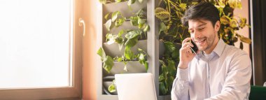 Küçük işletme geliştirme. Dizüstü bilgisayar üzerinde çalışan ve kafede telefonla konuşan neşeli işadamı, boş alan