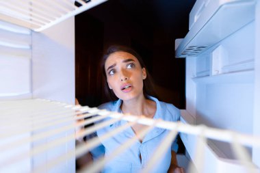 Yiyecek için para sıkıntısı. Evdeki karantina sırasında buzdolabının boş raflarına bakan genç bir kadın.