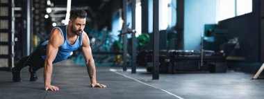 Mavi kolsuz tişörtlü bir adam şınav çeker, iyi donanımlı bir spor salonunda zindelik ve güç gösterisi yapar, uzayı taklit eder.