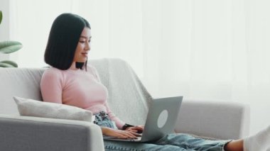 Modern hafta sonu aktiviteleri. Asyalı tatlı bir bayan internette boş vakit geçiriyor, bilgisayarla sohbet ediyor, evdeki kanepede oturuyor, ağır çekimde.