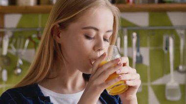 Güne vitaminlerle başla. Neşeli kız mutfakta taze portakal suyu içiyor.