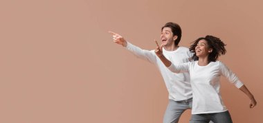 Cool offer. Joyful multiracial couple pointing at copy space and jumping over yellow background in studio, full length shot