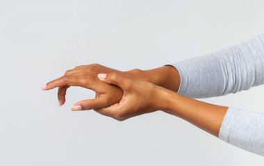 Gri arka planda el eklemlerine masaj yapan, cep telefonu kullanmaktan acı çeken Afrikalı genç bir kadın.