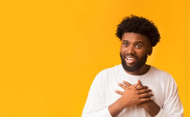 Şaşırmış siyah adam elleriyle göğsüne dokunuyor, sevimli bir şey görüyor, turuncu arka plan.