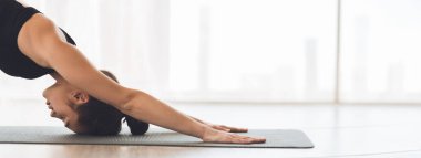 Bir kadın, güneşte yoga stüdyosunda nefesine odaklanmış, yere bakan köpek duruşunu takınır.