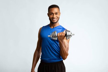 Ağırlık kaldırma. Arkadaş canlısı afro koç, sarı stüdyo duvarına izole edilmiş dambıl ile kaslarını şişiriyor.