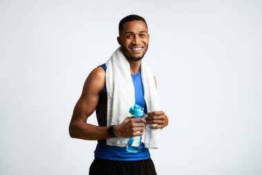 Susuz kalma. Boynunda havluyla sarı stüdyo arka planında su şişesi tutan kaslı zenci adam portresi.