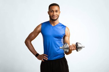 Kuvvet kavramı. Sarı stüdyo duvarına izole edilmiş dambıllarla çalışan gülümseyen afro bir adam.