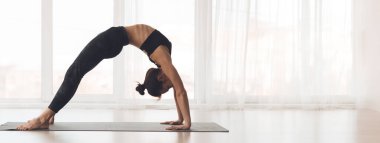 Köprü pozu veren bir kadın, yoga minderinde denge kurarken sırtını zarifçe eğiyor.