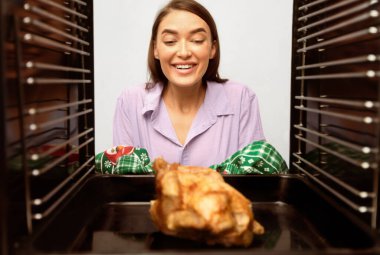 Lezzetli bir yemek. Mutlu genç ev hanımı fırından leziz kızarmış tavuk, içeriden manzara alıyor.
