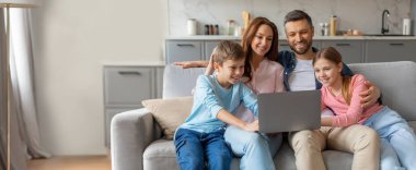 Dört kişilik bir aile oturma odalarındaki bir kanepede rahatça oturup dizüstü bilgisayarda film izliyor. Gülüşlerini ve gülüşlerini paylaşıyorlar, evlerinde rahat bir atmosfer yaratıyorlar..