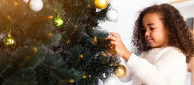 Sevimli küçük Afrikalı kız Noel ağacını renkli cam süslemelerle süslüyor.