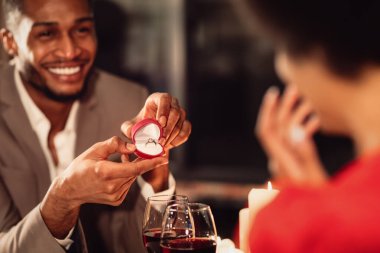 Sevgililer Günü Teklifi. Mutlu Afro Adam, Restoranda romantik bir randevu sırasında kız arkadaşına nişan yüzüğü veriyor ve evlenme teklif ediyor.