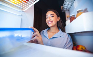 Diyet programı. Neşeli kız yemek kabını buzdolabından alıyor, manzarası da içeriden.