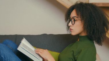 Faydalı bilgi. Gözlüklü genç Afro-Amerikan kadının profil portresi. Kitap okuyor ve düşünüyor.