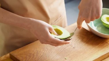 Kadın avokadoyu kaşıkla alıyor ve kaseye koyuyor. Sağlıklı vejetaryen yemekleri