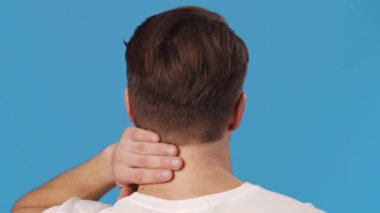 Ofis sendromu. Adamın iltihaplı boynuna, mavi stüdyo geçmişine, yavaş çekimde masaj yaptığı arka plan görüntüsü.