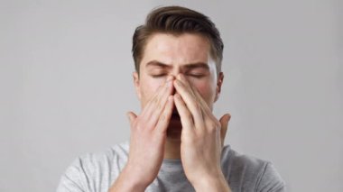 Sinüzit sorunu. Burnu ağrıyan, gri stüdyo arkaplanı, ağır çekim genç hasta adamın portresini yakın çekimde çek.