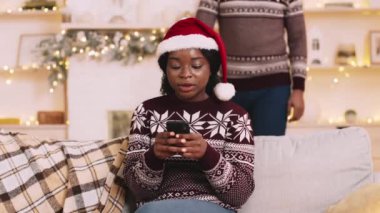 En iyi Noel sürprizi. Siyah kadın cep telefonuyla iletişim kuruyor, erkek ona sürpriz yapıyor, elleri olan kadının gözlerini kapıyor. Xmas birlikte kutlama konsepti