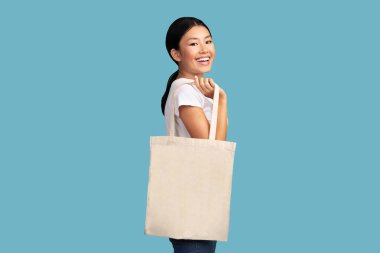 Smiling Asian Girl Holding White Eco Tote Bag Smiling Standing Over Turquoise Studio Background. Ecology And Eco-Friendly Lifestyle Concept.